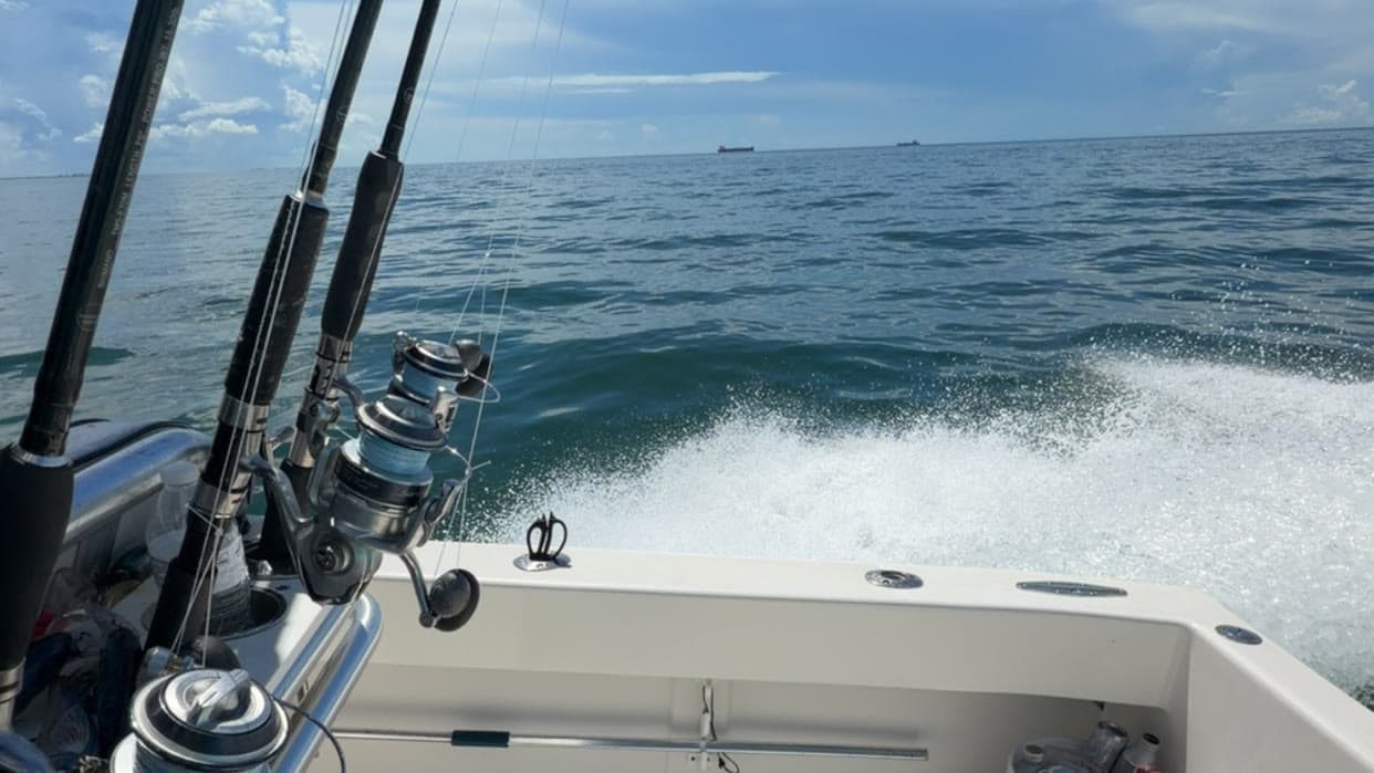 Fishing rods in holders on a center console running offshore, with a white wake behind the boat