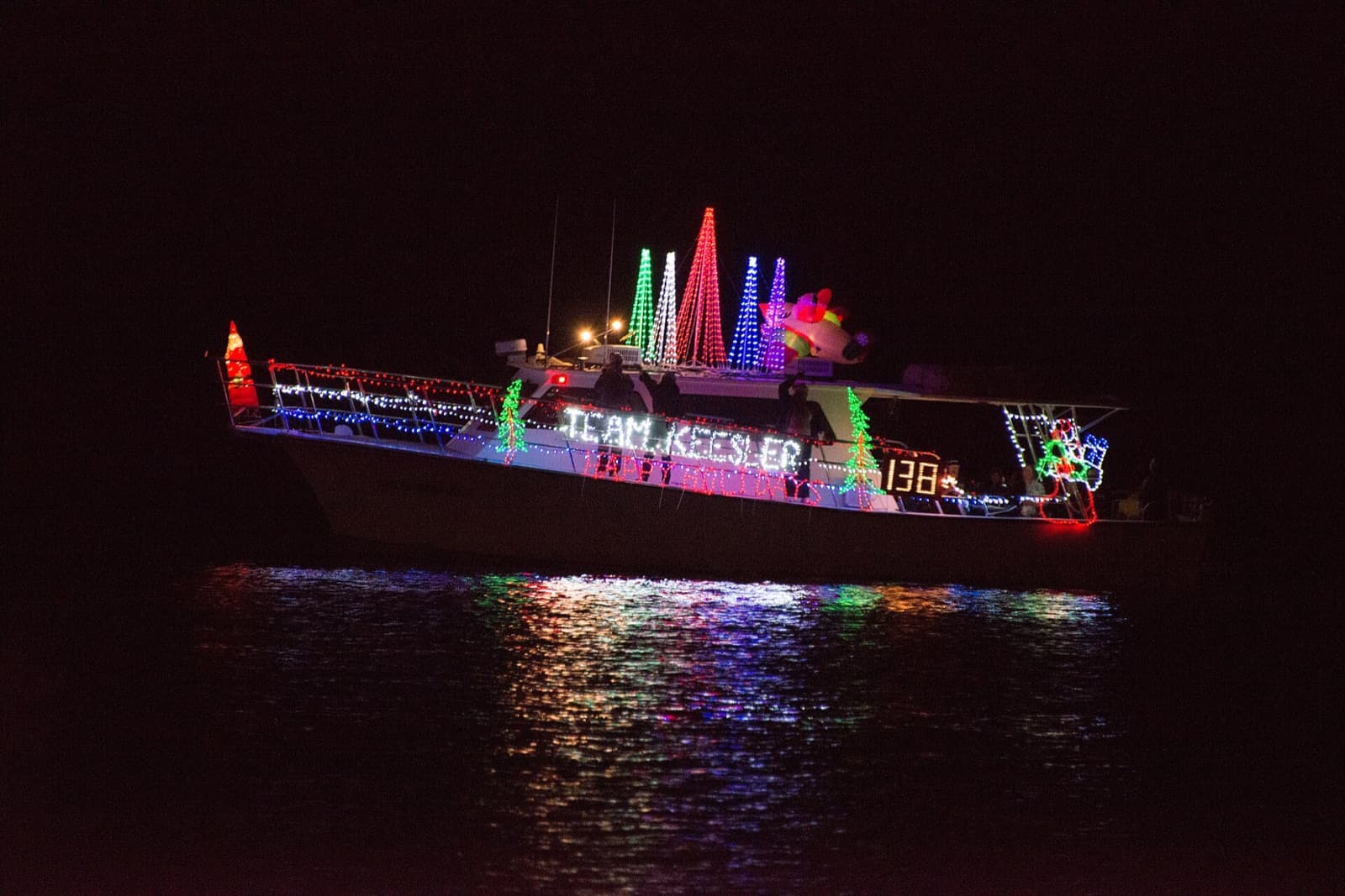 Cabin cruiser strung with holiday lights and lit trees, showing a lighted entry number on its side