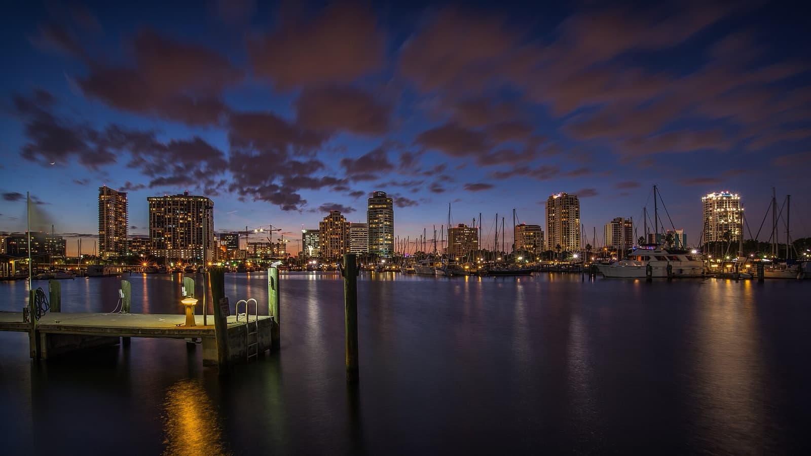 Downtown St. Petersburg skyline and marina sailboats at dusk, seen from a wooden dock